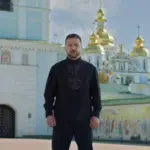 Володимир Зеленський у чорній вишиванці з довгими рукавами та сірою вишивкою з геометричним орнаментом на тлі Михайлівського